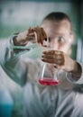 Chemical laboratory. Young blonde woman holding two flasks with liquid in it. About to transfuse the liquid. Focus on