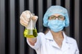 Chemist examining test tube with substance. She`s in protective uniform over grey abstract grey background Royalty Free Stock Photo