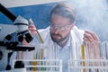 Chemist in goggles with reagents in tubes and microscope in laboratory