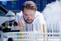 Chemist in goggles with reagents in tubes and microscope in laboratory