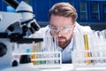 Chemist in goggles with reagents in tubes and microscope in laboratory