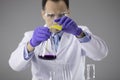 Chemist researcher in blue gloves and glasses pouring colorful liquids in flask