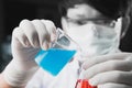 Chemist student boy pouring blue liquid in beger glass to erlenmeyer flask chemistry with red liquid on biochemical experiment.