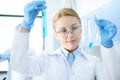 Chemist in white coat holding test tubes with reagents and making experiment