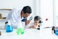 .In chemistry classroom with many laboratory tools. A little Asian girl writing data experiment into textbook and male teacher Royalty Free Stock Photo