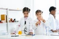 In chemistry classroom with many laboratory tools. Students and teacher do experiment together. Two little Asian girls help each Royalty Free Stock Photo