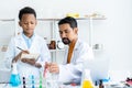 In chemistry classroom with many laboratory tools on table. A young African boy and male teacher in white lab coat Royalty Free Stock Photo