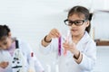 In chemistry classroom with many laboratory tools. Two little Asian girl in white lab coat help each other for experiment. A girl Royalty Free Stock Photo