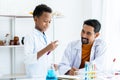 In chemistry classroom with many laboratory tools. A young African boy with teacher in white lab coat do experiment together. A