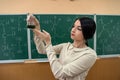 Chemistry female teacher observing reaction test-tube at classroom and against green blackboard