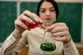 Chemistry female teacher observing reaction test-tube at classroom and against green blackboard