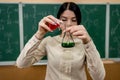 Chemistry female teacher observing reaction test-tube at classroom and against green blackboard