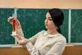 Chemistry female teacher observing reaction test-tube at classroom and against green blackboard