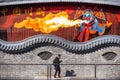 Man walking by a painted fresco of a fire spitter chinese opera artist