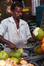 An Indian man cuts a young green coconut with a sharp chopper for coconut water juice in the city-center of Chennai.