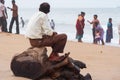 A man sitting on a tree stump gazes towards the rough sea as other people enjoy themselves at Marina Beach in Chennai.