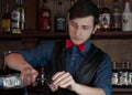 Barman standing at bar counter and pouring alcoholic drink from bottle into glass