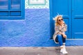 Chererful and relaxed beautiful woman sit down outside a colorful blue house in the street - home properties owner people concept