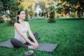 Cherful nice young woman stretching legs on yoga mate outside in park. She smiles and hold hands on feet.