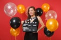 Cherful young girl in black dress celebrating, holding classic black film making clapperboard on bright red background