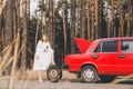 Chernigov, Ukraine - November 10, 2020: Girl in a white wedding dress near the car. The girl and the spare tire. Red retro car in