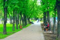 City park with promenade path benches and green trees. People have a rest in city park