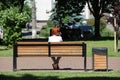Redhead girl sitting on bench in city park and talking on phone