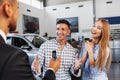 Cherrful young couple at the dealership buying a new car