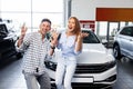 Cherrful young couple at the dealership buying a new car