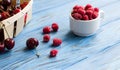 Cherries in basket, raspberries in cup on blue wooden background Royalty Free Stock Photo
