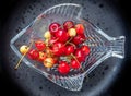 Cherries of varying degrees of greenness in a decorative glass vase on a dark background close-up