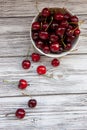 Cherry berries in a white Cup, scattered cherry berries on a light wooden background, flat fly Royalty Free Stock Photo