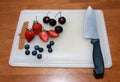 Cherry, berry fruit, strawberry and chopped strawberry with knife on the white chopping board on the wooden table.