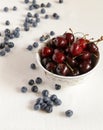 Cherry in a bowl on a table, lies bilberry nearby.