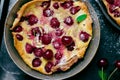 Cherry Dutch Baby, Puff German Pancake on Vintage Pans and Dark Background, Homemade Summer Dessert