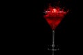 Cherry falling into splashing cocktail in martini glass isolated on black