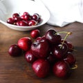Cherry fruits. Dark red berries in a white plate and scattered on a wooden table. Royalty Free Stock Photo