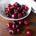 Cherry fruits. Dark red berries in a white plate and scattered on a wooden table. Royalty Free Stock Photo