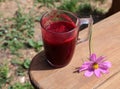 Cherry juice in a mug on the edge of a wooden table in the open air with a pink flower, side view-the concept of cooling drinks in Royalty Free Stock Photo