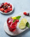 Cherry-lime mojito cocktail with mint, lime and ice on a marble board on a blue background