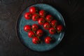 Cherry tomato branch, fresh ripe organic vegetables in blue green plate on dark black textured background Royalty Free Stock Photo