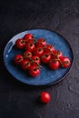 Cherry tomato branch, fresh ripe organic vegetables in blue plate on dark black textured background Royalty Free Stock Photo