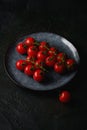 Cherry tomato branch, fresh ripe organic vegetables in grey plate on dark black textured background Royalty Free Stock Photo