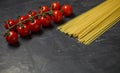 Cherry tomatoes branch and raw spaghetti - ingredients for making Italian pasta, on dark background, selective focus Royalty Free Stock Photo
