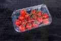 Cherry tomatoes clusters in closed plastic packaging on black surface