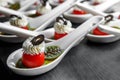 Cherry tomatoes on dessert spoons, garnished with buttercream and sliced olives