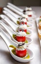 Cherry tomatoes on dessert spoons, garnished with buttercream and sliced olives