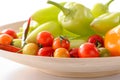 Cherry tomatoes, red chili pepper and green bell peppers on wooden dish close-up against white background Royalty Free Stock Photo