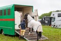 Young female horse rider putting her horse into horsebox assisted by older female