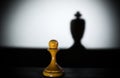 A chess pawn casting a king piece shadow in dark concept of strength plus aspirations